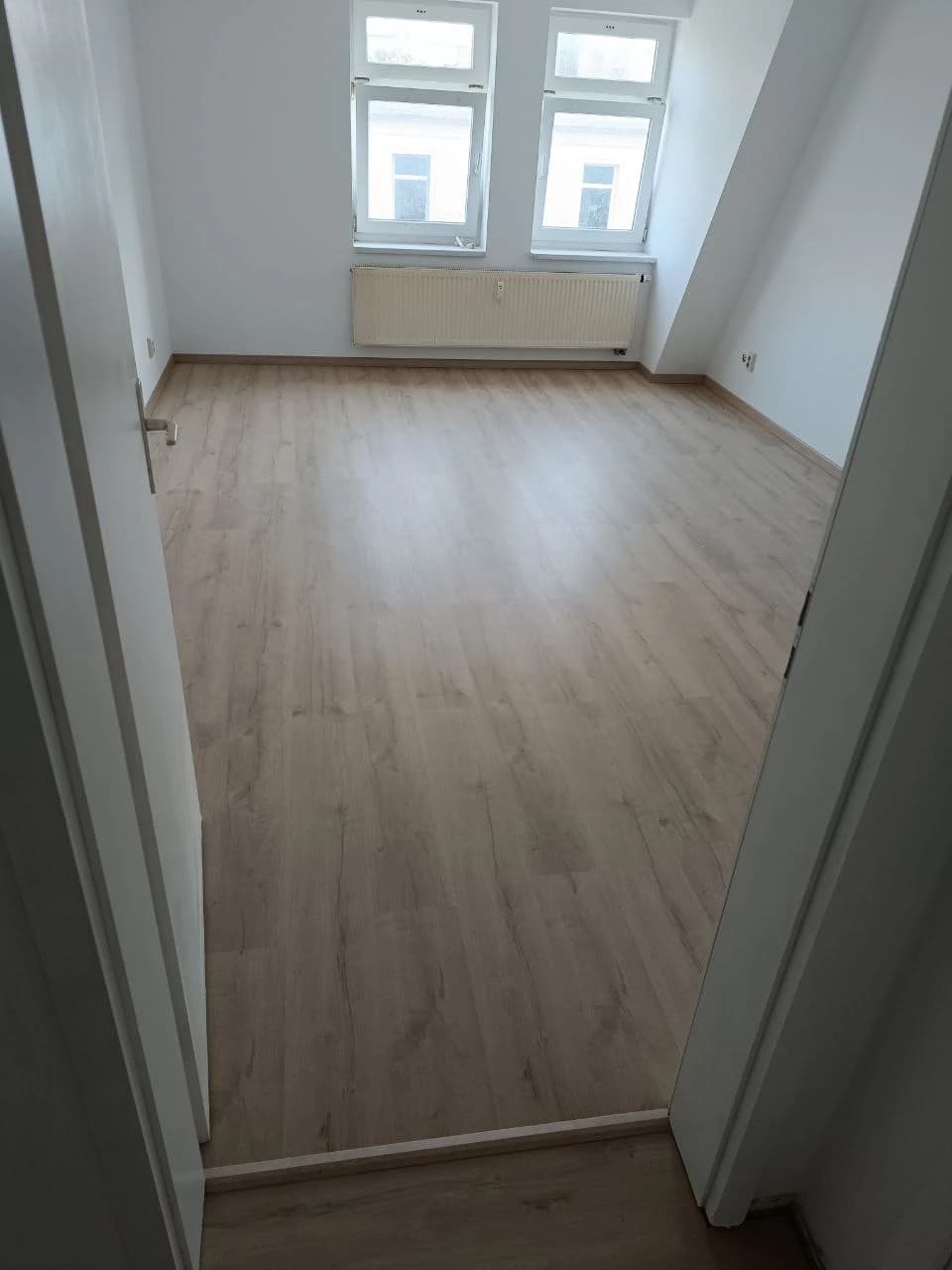 Zimmer nach der Renovierung mit hellem Laminat und Sockelleisten