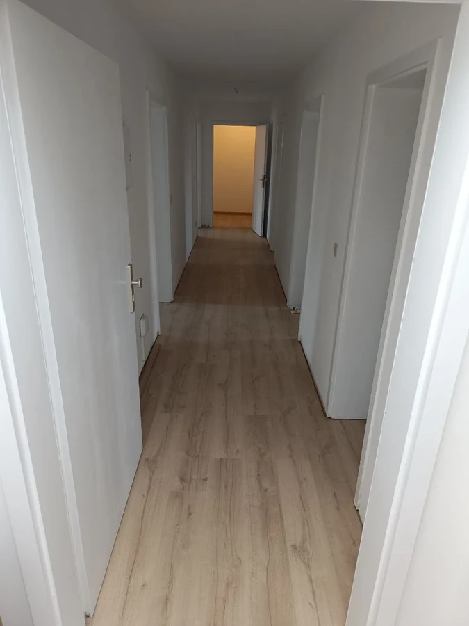 Flur nach der Renovierung mit hellem Laminat und weißen Wänden