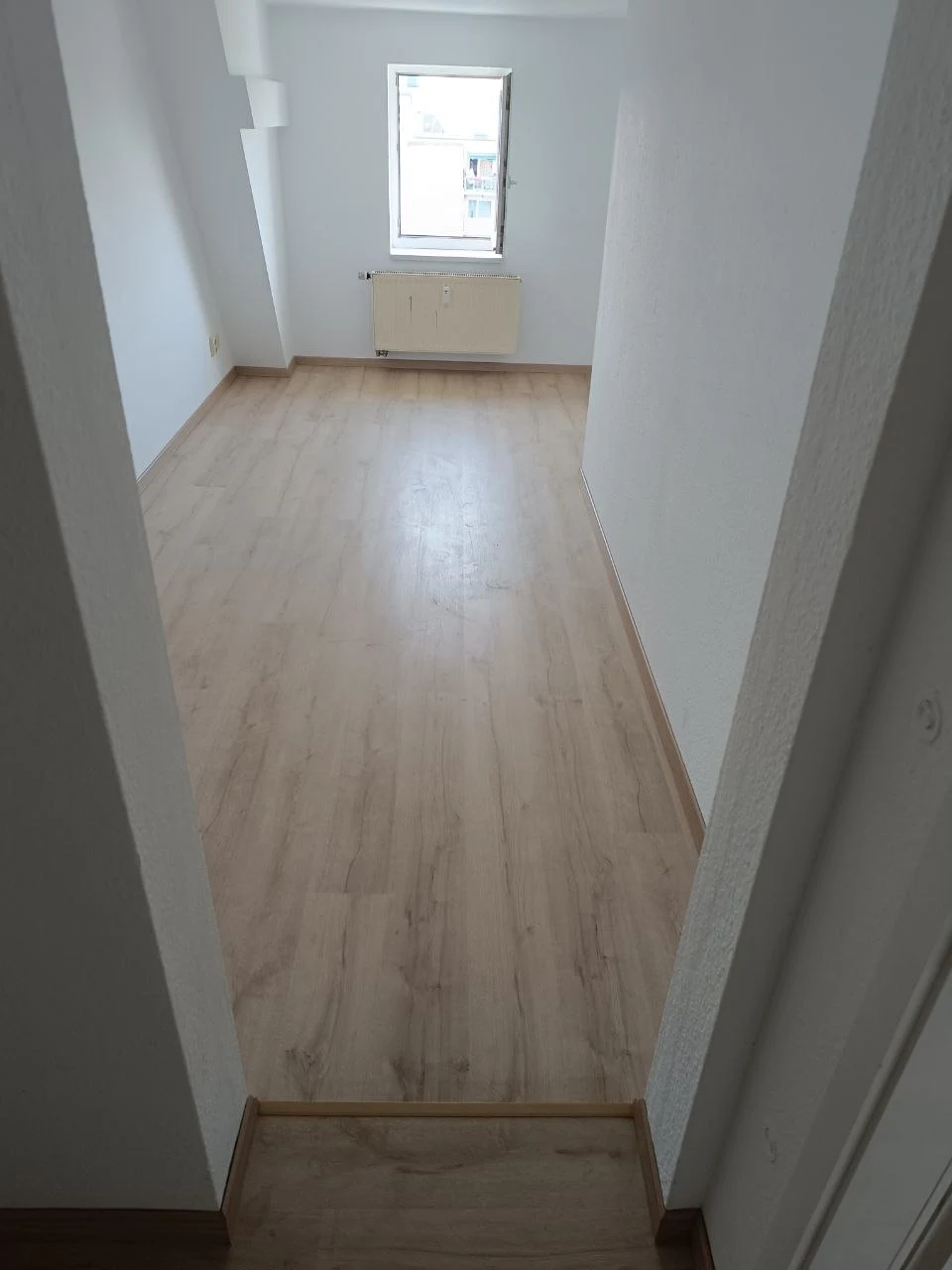 Renoviertes Zimmer mit hellem Laminat, weißen Wänden und Decke